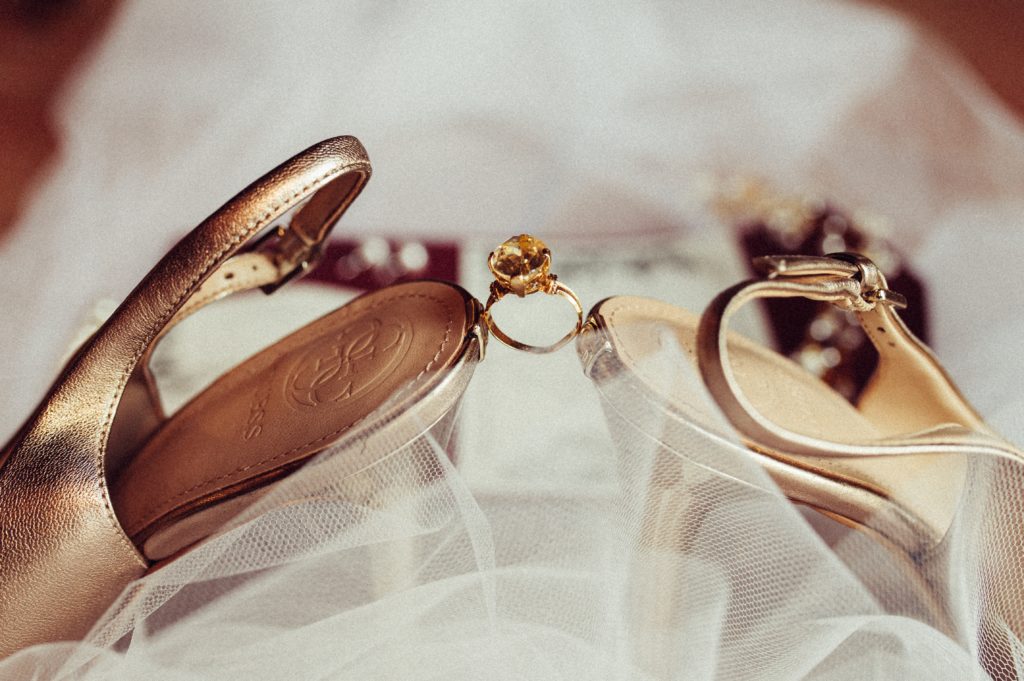 A wedding ring sits perched between the backs of two high-heeled shoes.